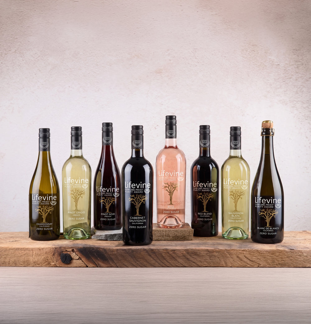 A lineup of eight Lifevine wine bottles in various colors, including white, red, rosé, and sparkling, arranged on a rustic wooden shelf against a textured beige wall.